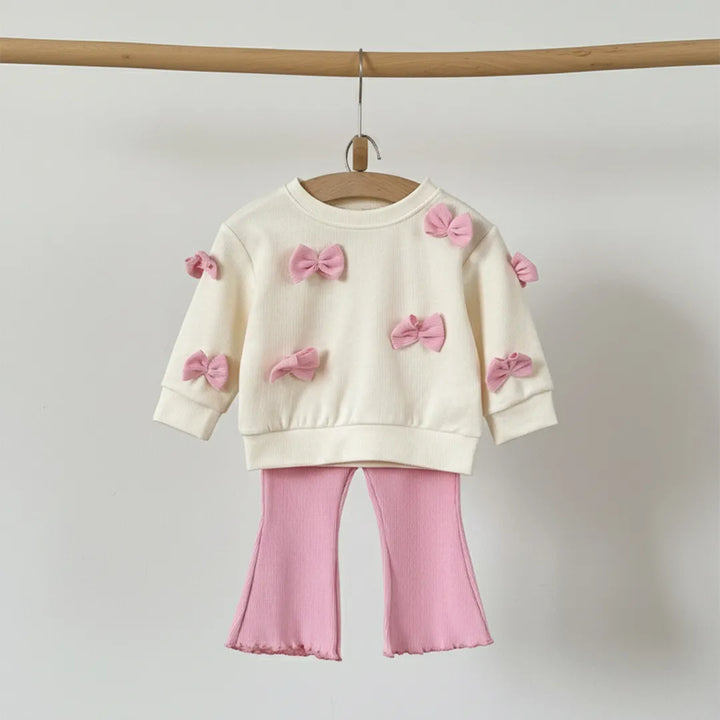 Children's outfit with cream sweater and pink pants on a wooden hanger against a light gray background