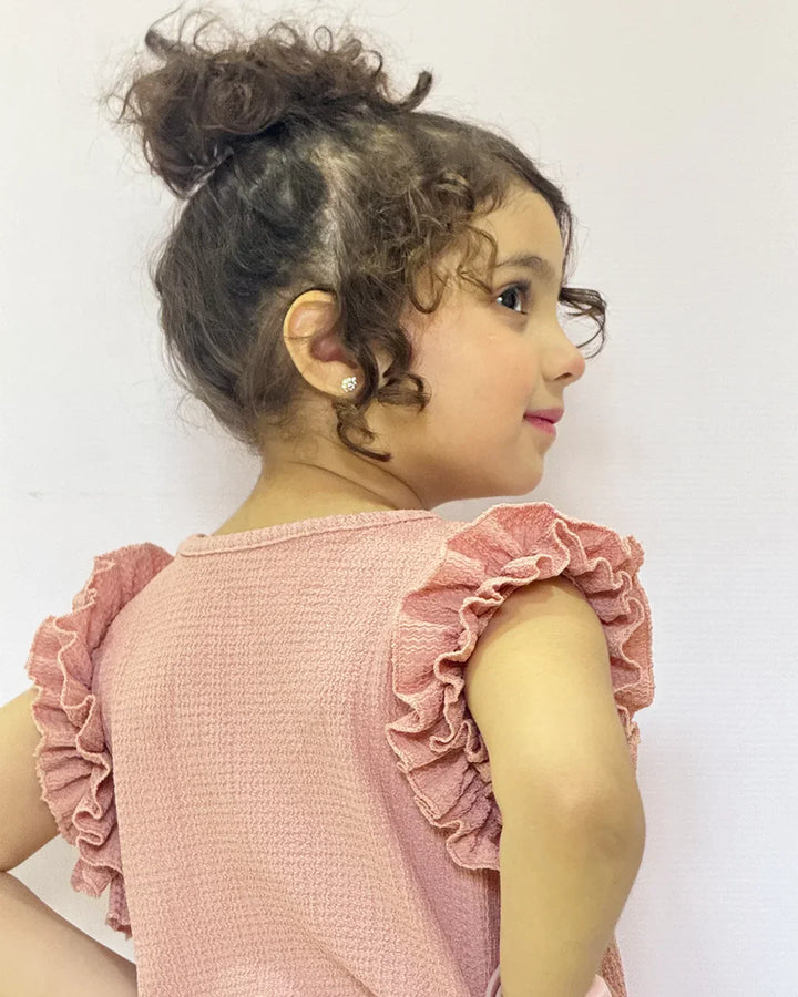 Young girl wearing a pink dress with ruffled sleeves against a white background