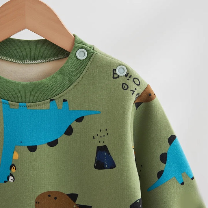 Green children's shirt with dinosaur print on a wooden hanger against a white background