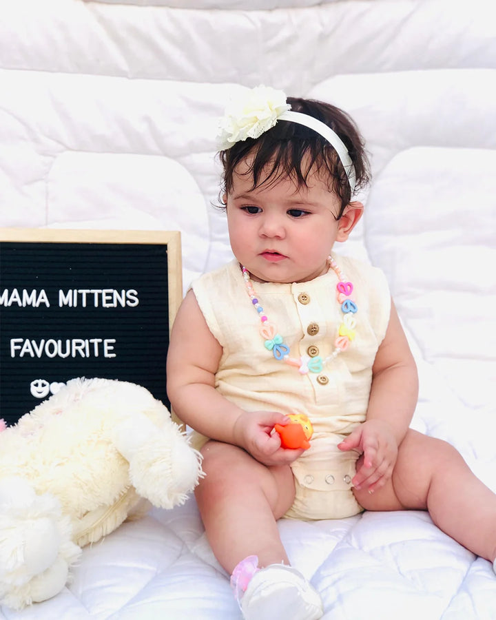 Baby sitting on a white blanket with a blackboard sign and teddy bear