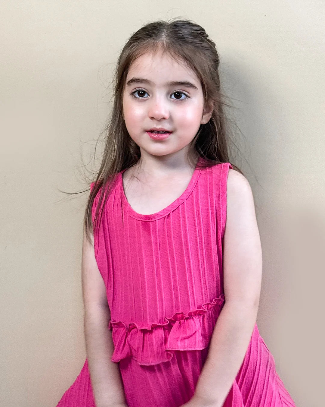 Young girl wearing a pink dress against a plain background