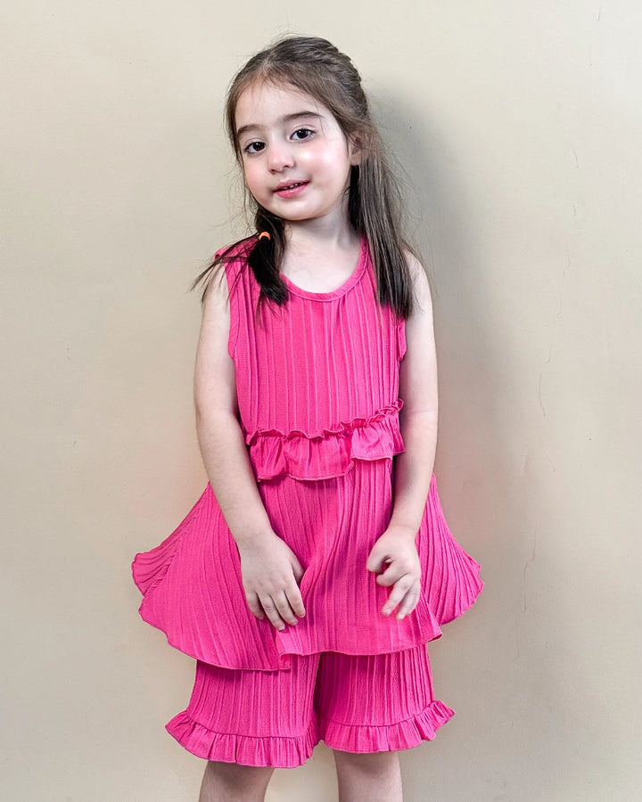 Young girl wearing a pink pleated dress against a plain background