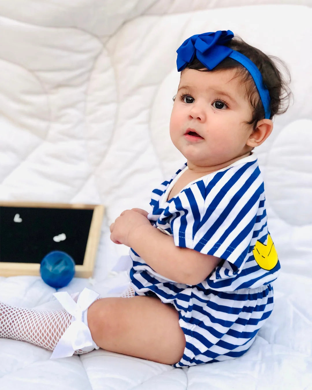 Baby in a blue and white striped outfit with a yellow heart on a white blanket.