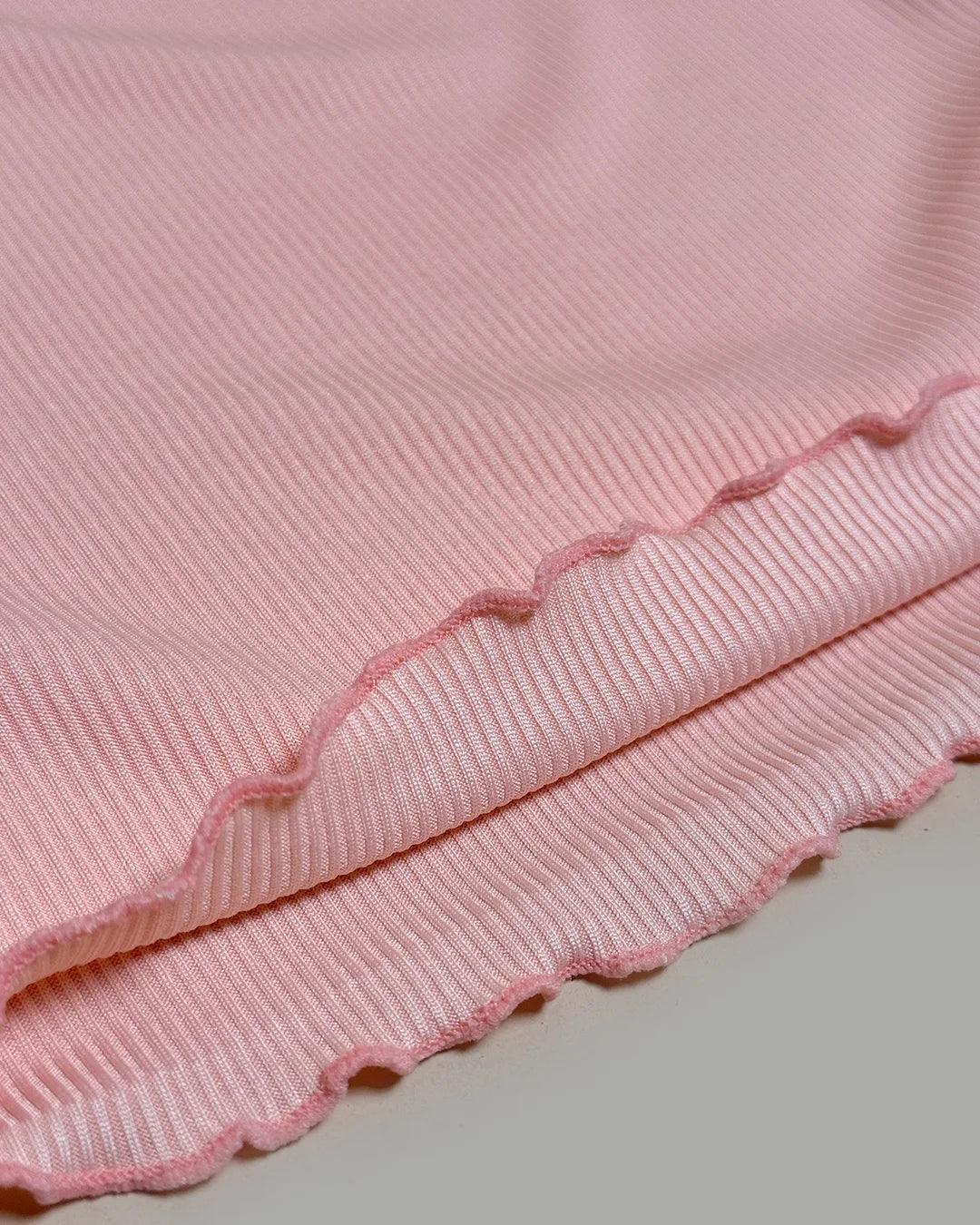 Close-up of a pink textured fabric with scalloped edge on a light gray background