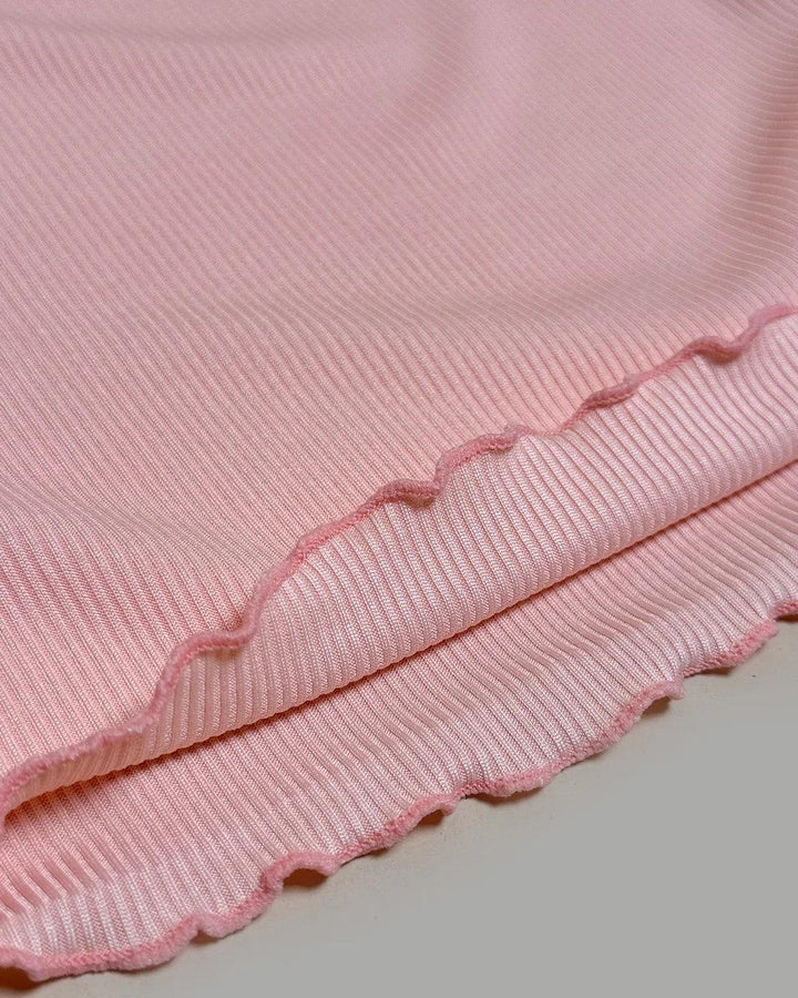 Close-up of a pink textured fabric with scalloped edge on a light gray background