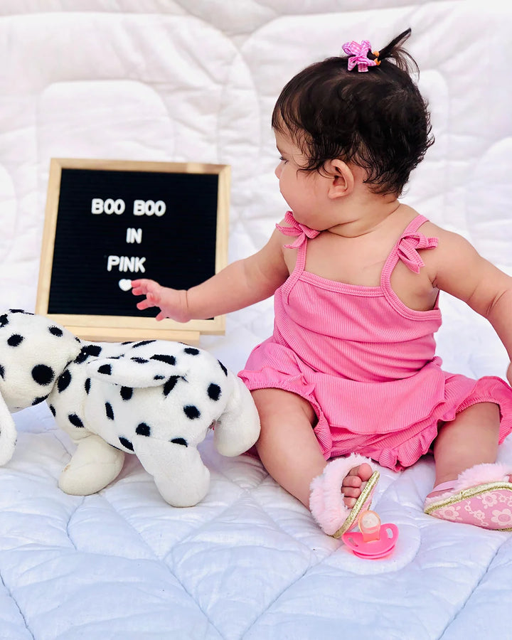Baby in pink outfit interacting with a letter board on a white blanket