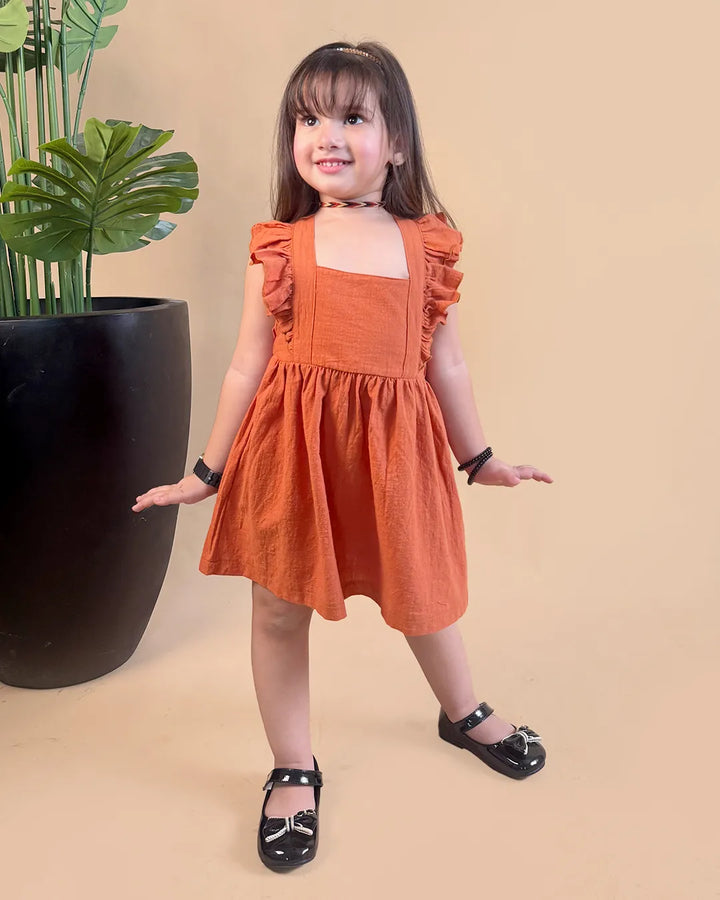baby girl in an orange dress standing next to a potted plant on a beige background