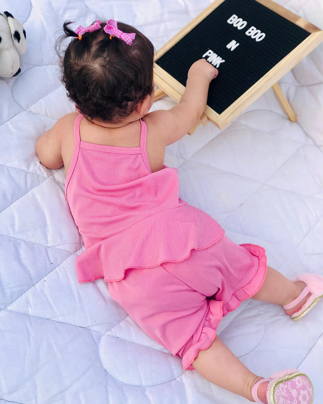 Child in pink outfit interacting with a letter board on a white blanket