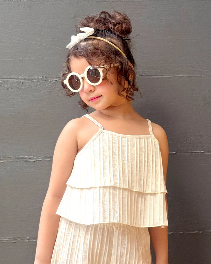 Young girl in a cream dress with sunglasses against a dark background