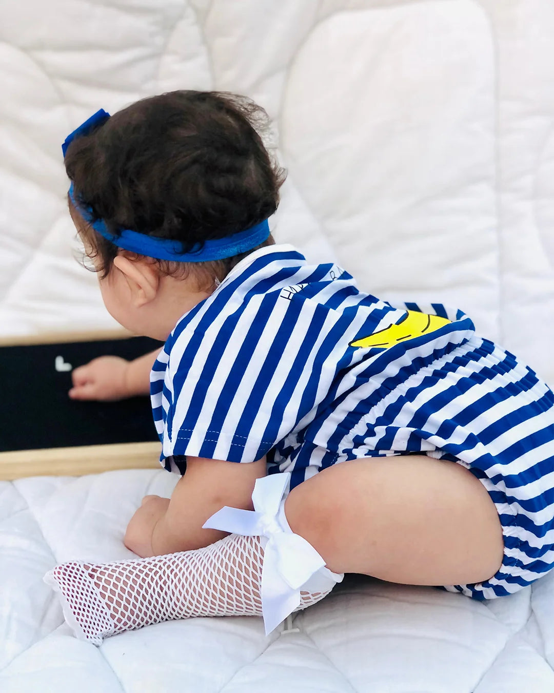 Child in a blue and white striped outfit with a yellow star, sitting on a bed.