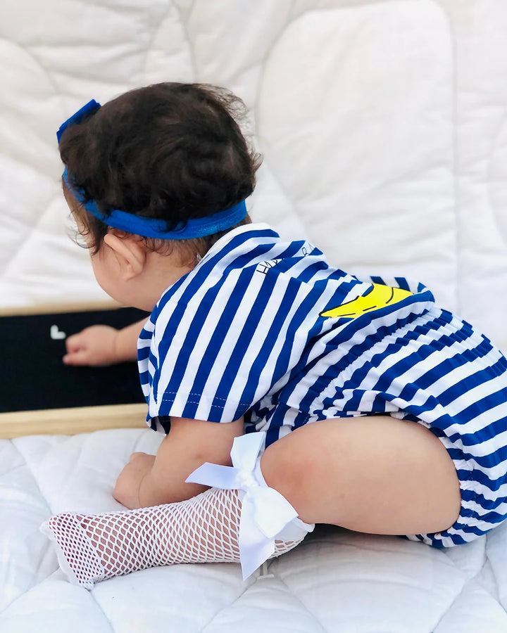 Child in a blue and white striped outfit with a yellow star, sitting on a bed.