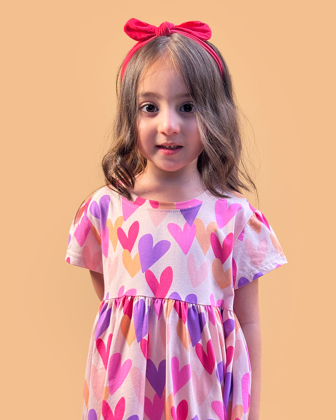 Young girl wearing a dress with colorful heart pattern against a beige background