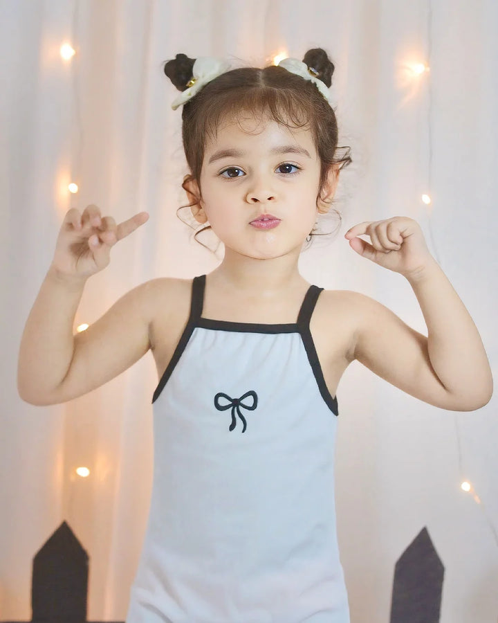 Child wearing a light blue swimsuit with a black bow design, standing against a soft, blurred background.