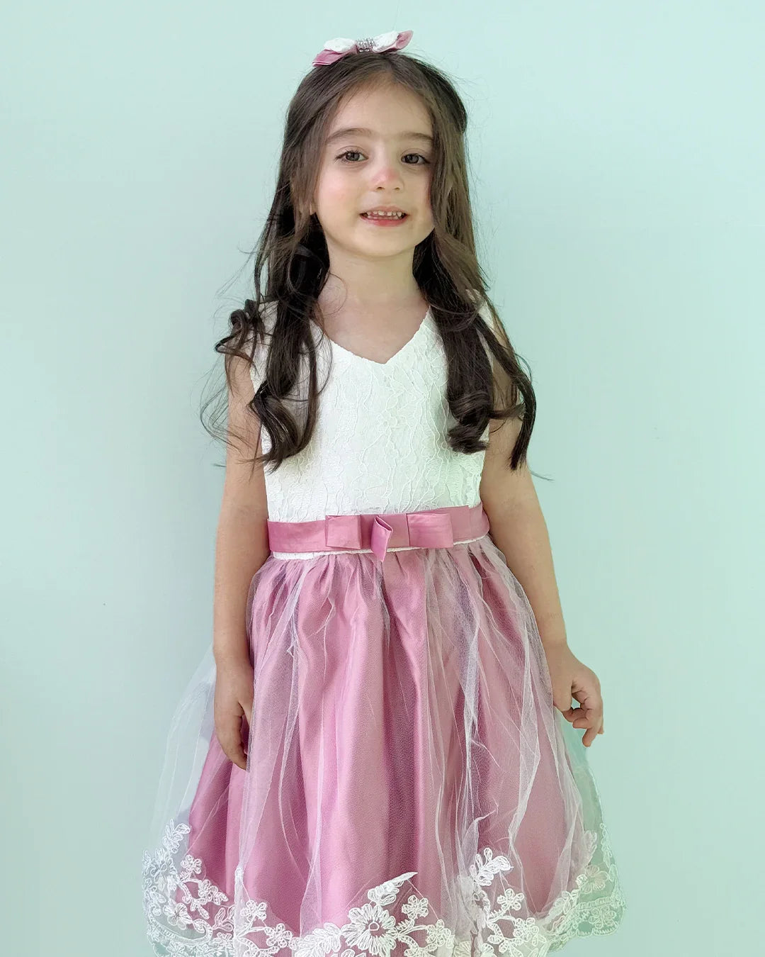 Young girl wearing a white top with pink ribbon and a pink skirt with lace trim on a light blue background