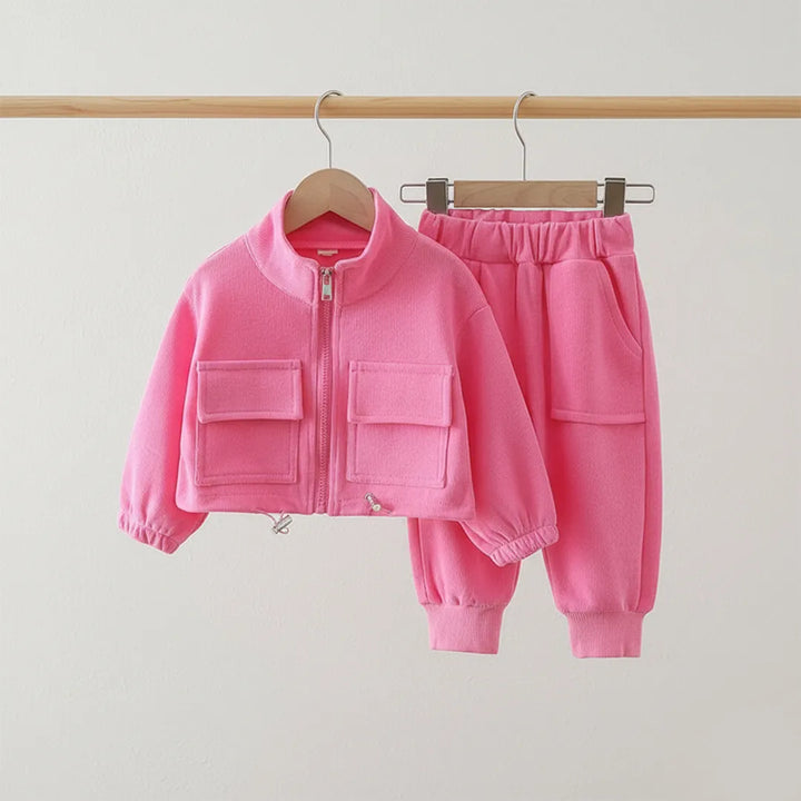 Pink children's jacket and pants set on hangers against a light gray background