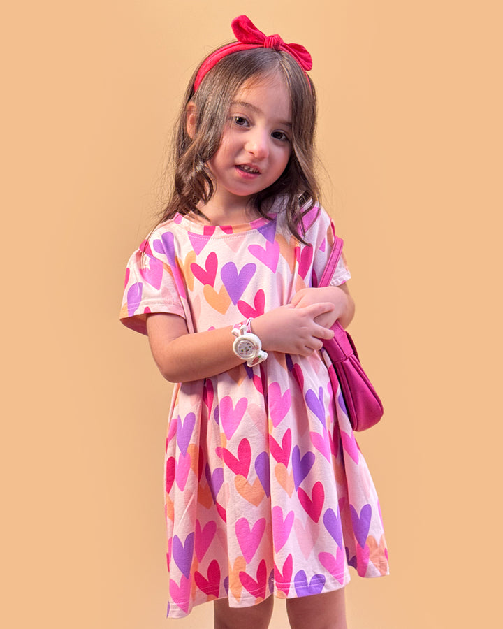 Young girl wearing a colorful heart-patterned dress with a pink headband and bag on a beige background