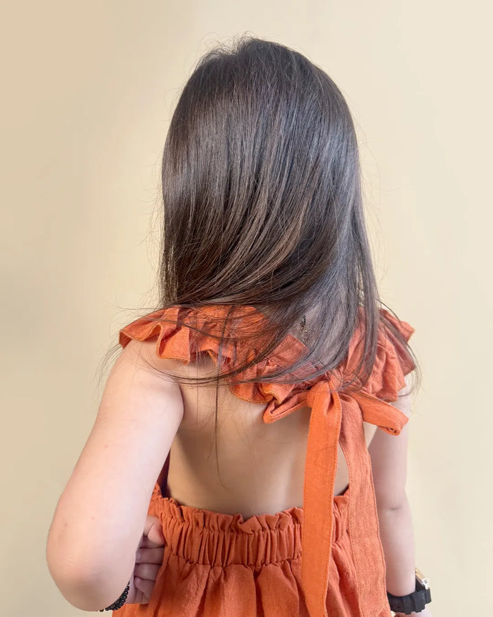 kid wearing an orange dress with ruffled straps against a beige background