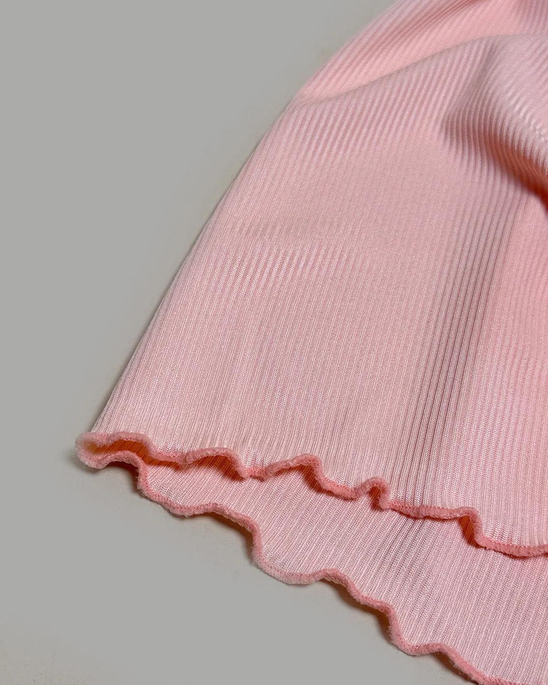 Close-up of a pink ribbed fabric with scalloped edge on a gray background