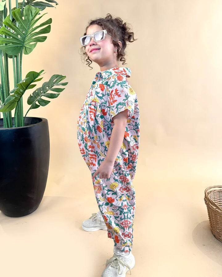 Child wearing a colorful floral outfit standing next to a plant on a beige background