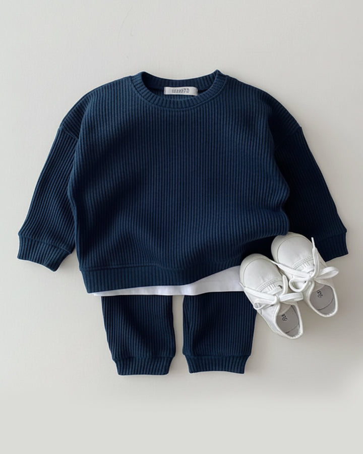 Navy blue sweater and pants set with white shoes on a light gray background