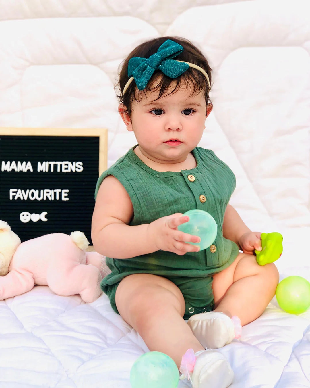 Baby in a green outfit with colorful toys and a sign in the background