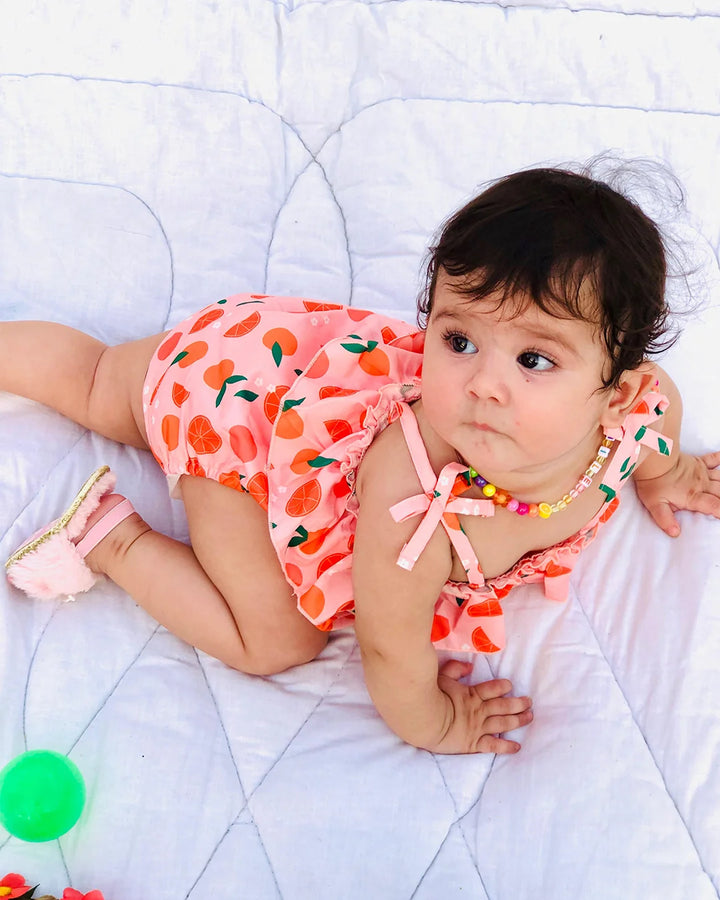Baby in a pink outfit with fruit pattern lying on a white blanket