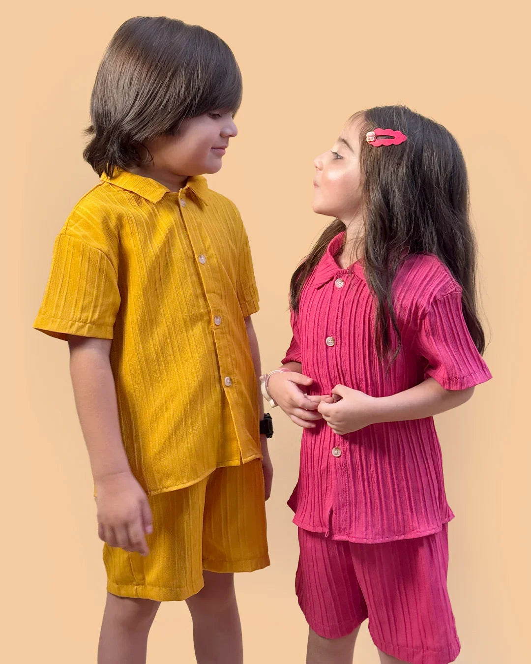 Two children wearing matching yellow and pink outfits against a beige background
