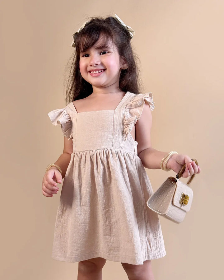 Young girl in a beige dress holding a small handbag against a beige background