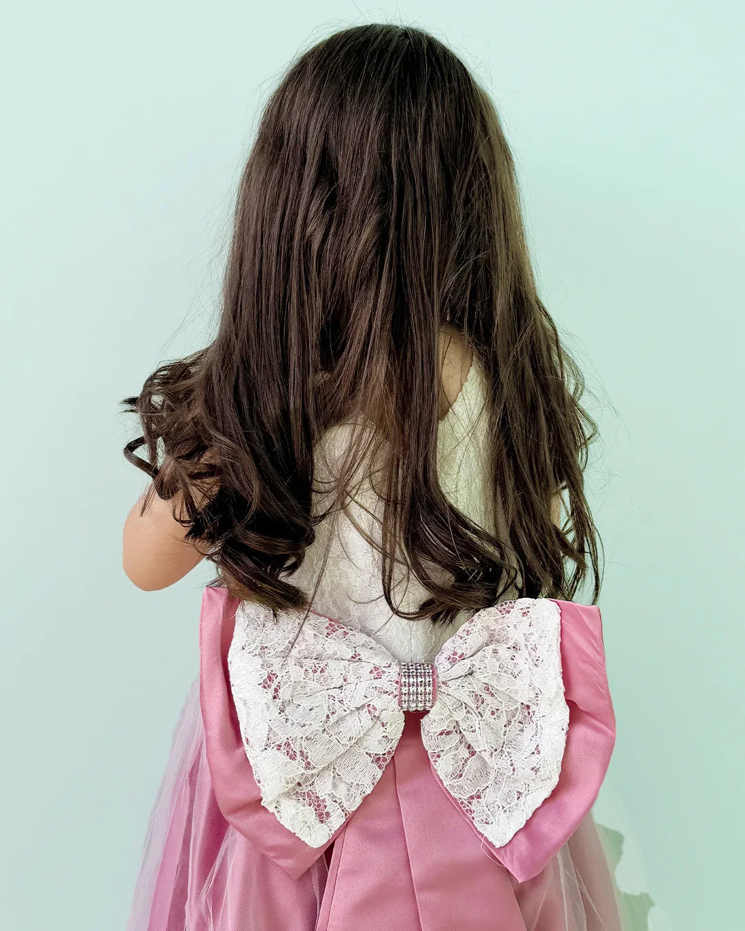 Person wearing a pink dress with a large lace bow on a light blue background