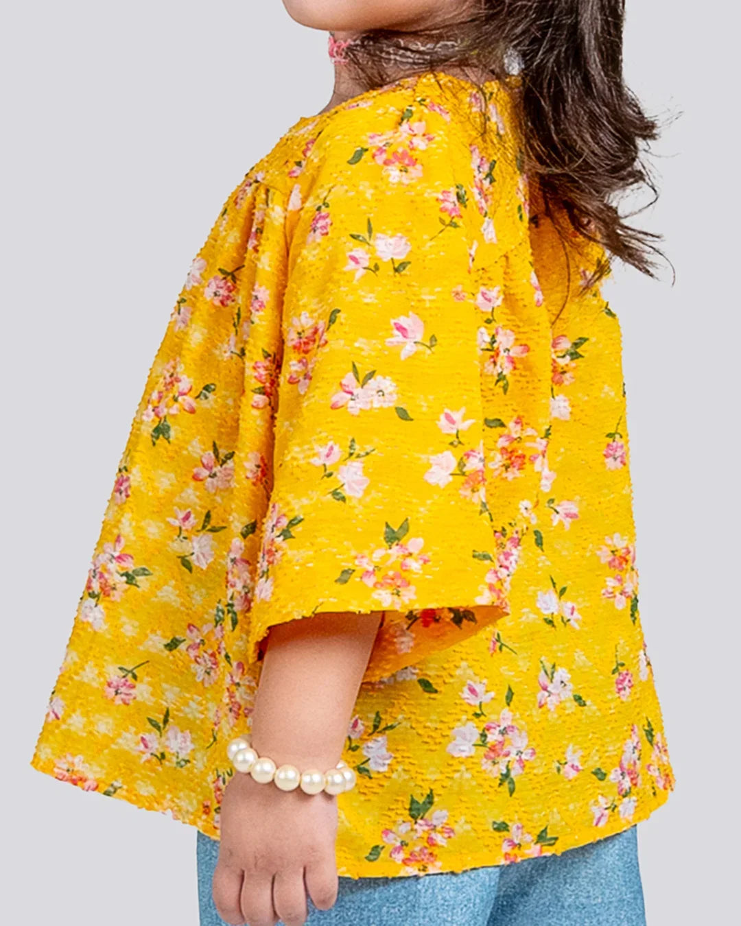 Person wearing a yellow floral kimono-style garment on a plain background