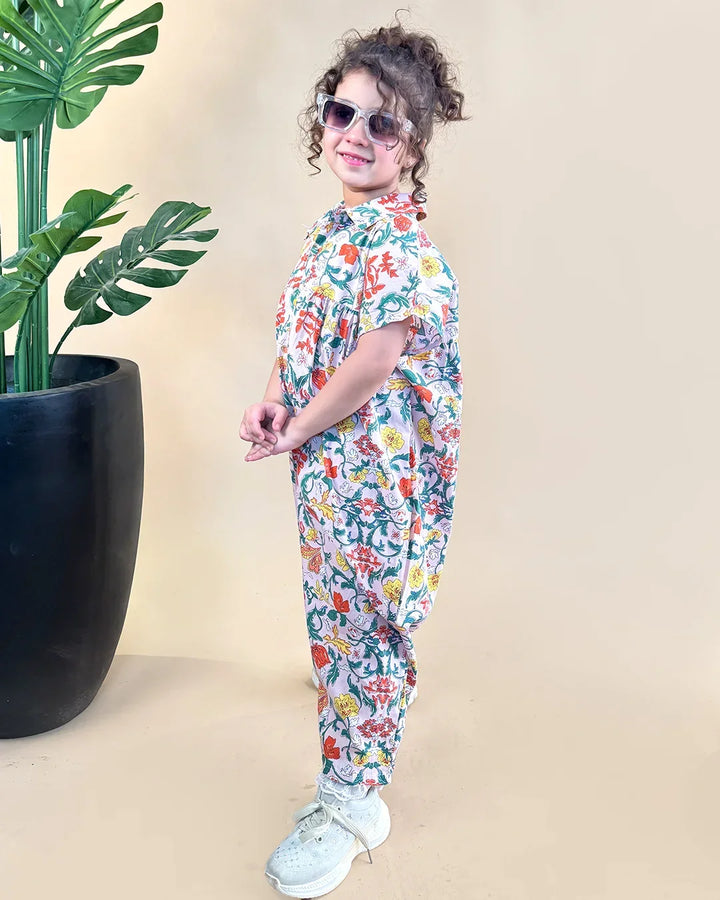 Child wearing a floral outfit standing next to a potted plant on a beige background