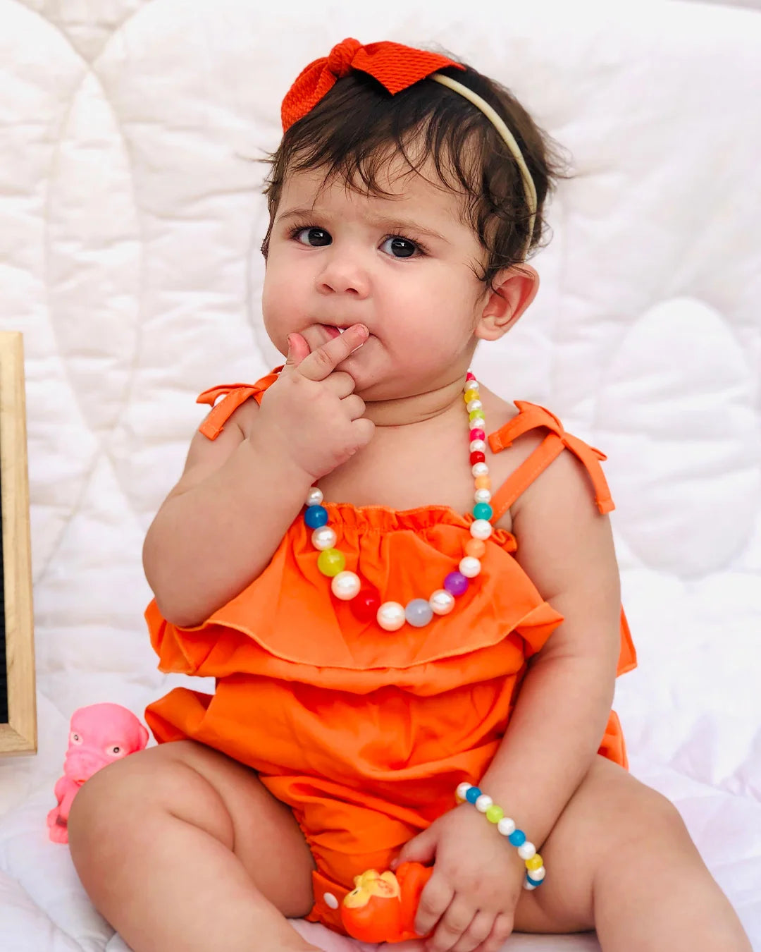 Baby in an orange outfit with colorful beads on a white background