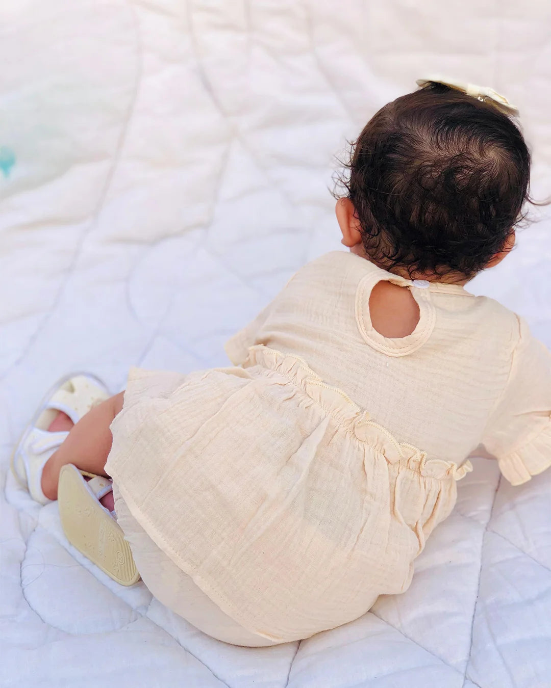 Baby in a cream-colored outfit lying on a white blanket