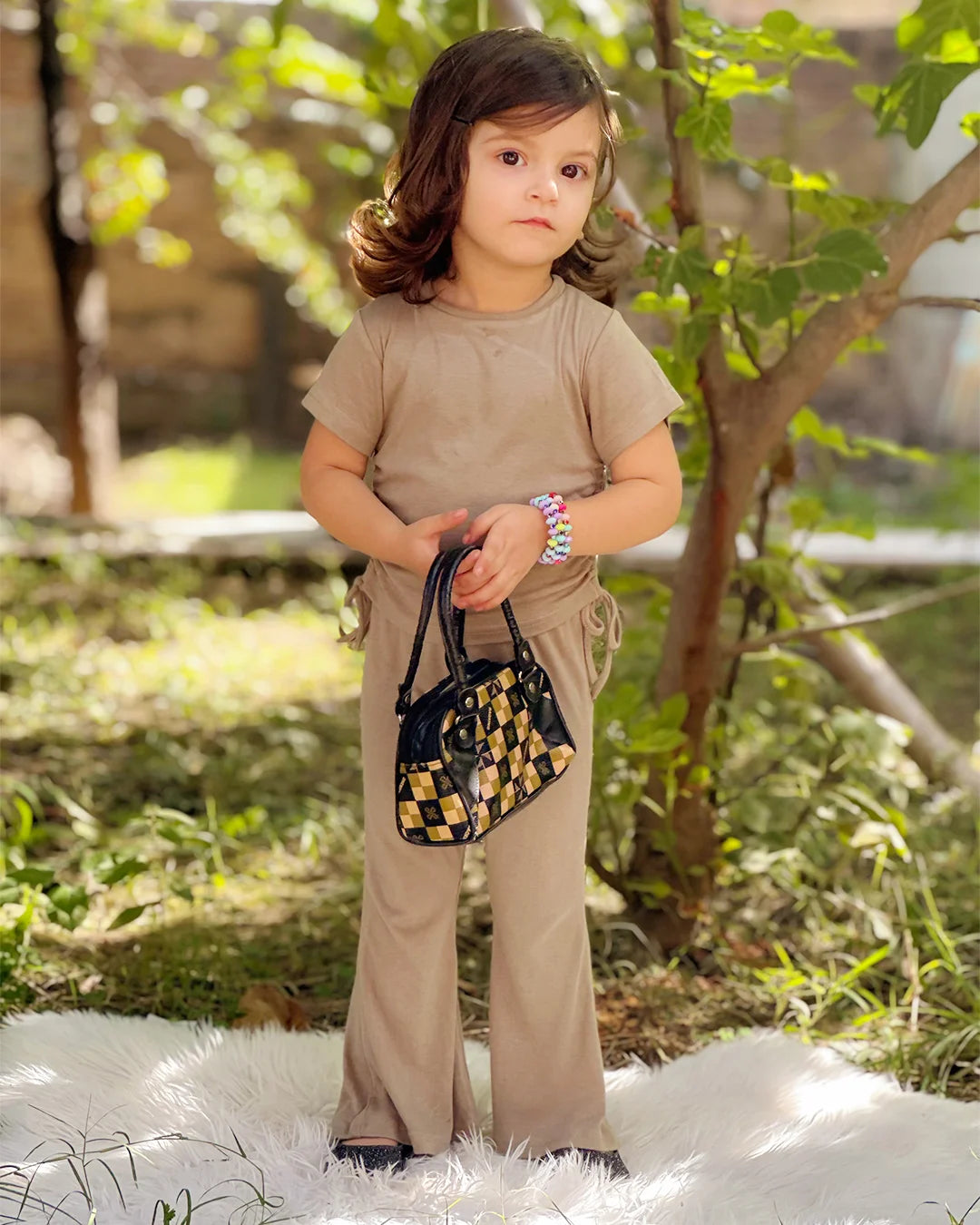 Child in beige outfit holding a small handbag outdoors