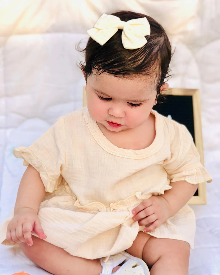 Baby in a light yellow outfit with a large bow headband on a soft white background