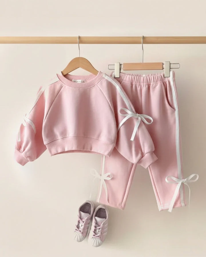 Pink children's outfit with matching shoes on a wooden hanger against a light background