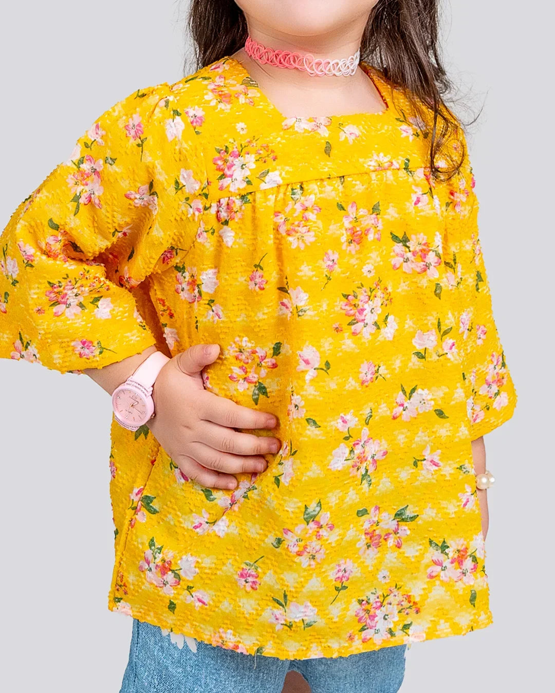 Child wearing a yellow floral dress on a plain background