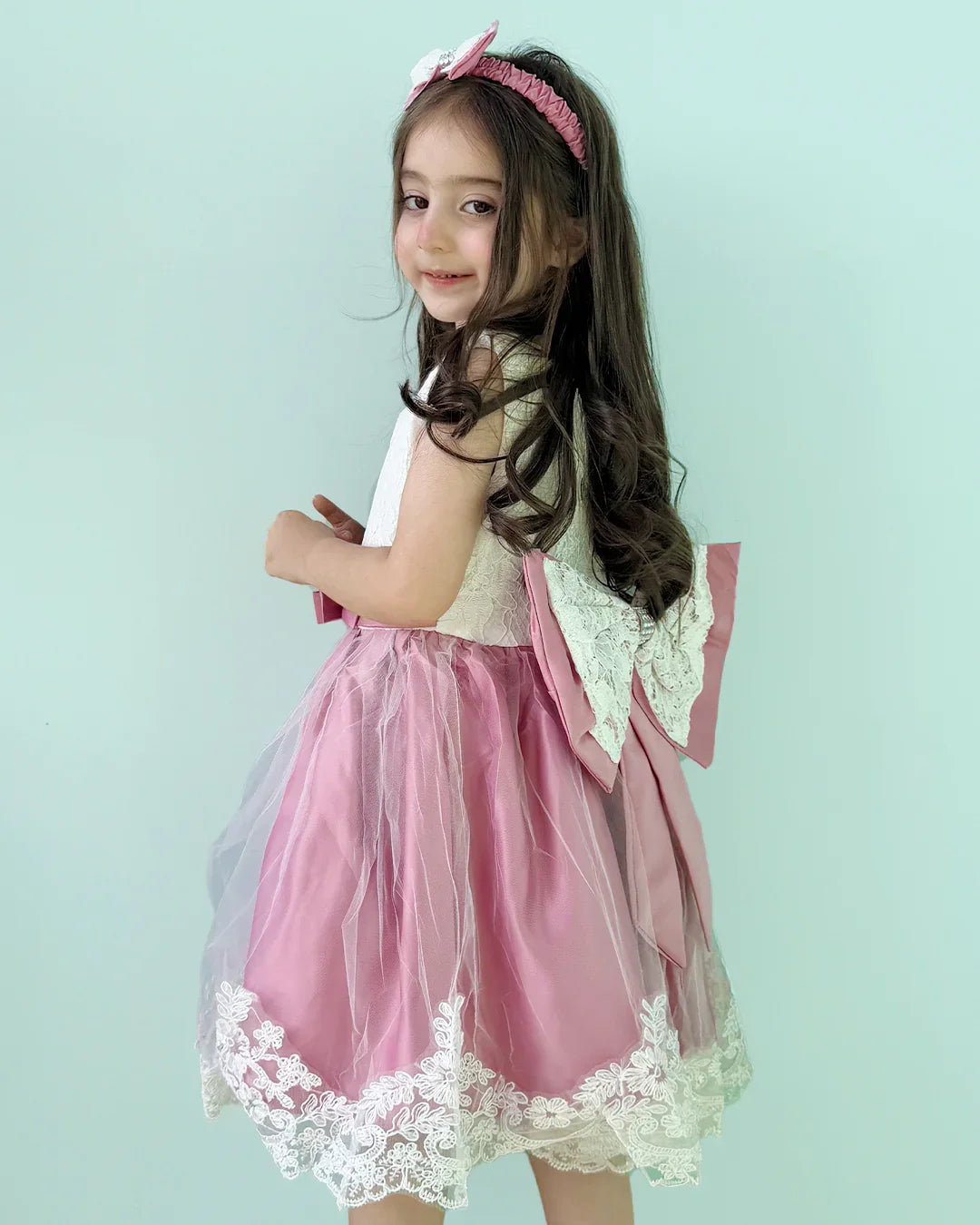 Young girl wearing a pink dress with lace details against a light blue background