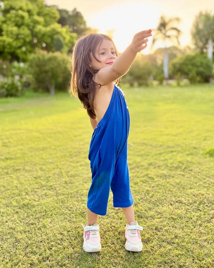Child in a blue dress standing on grass with trees in the background