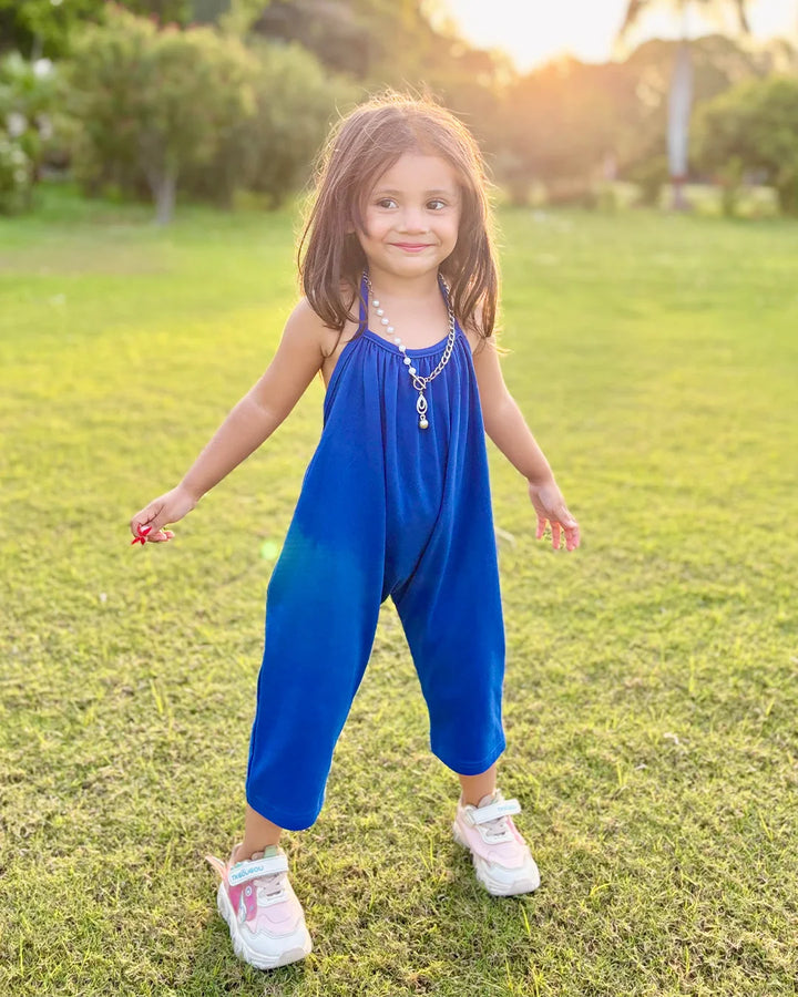 Young girl in a blue dress standing on grass with a sunset background