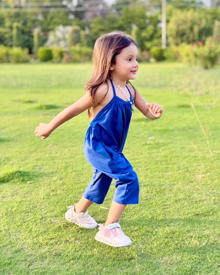 Young girl in a blue dress running on grass with trees in the background