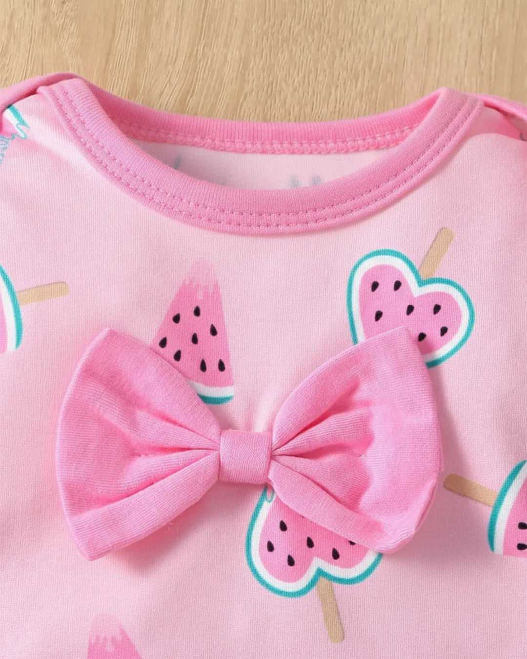 Pink outfit with a large bow and watermelon designs on a wooden surface