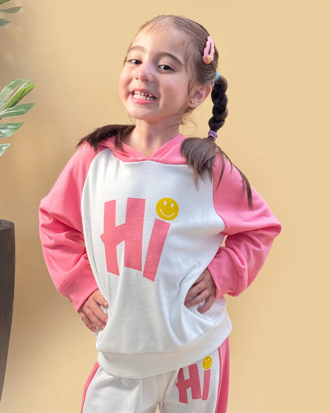 Child wearing a pink and white outfit with 'Hi' and smiley face design on a beige background