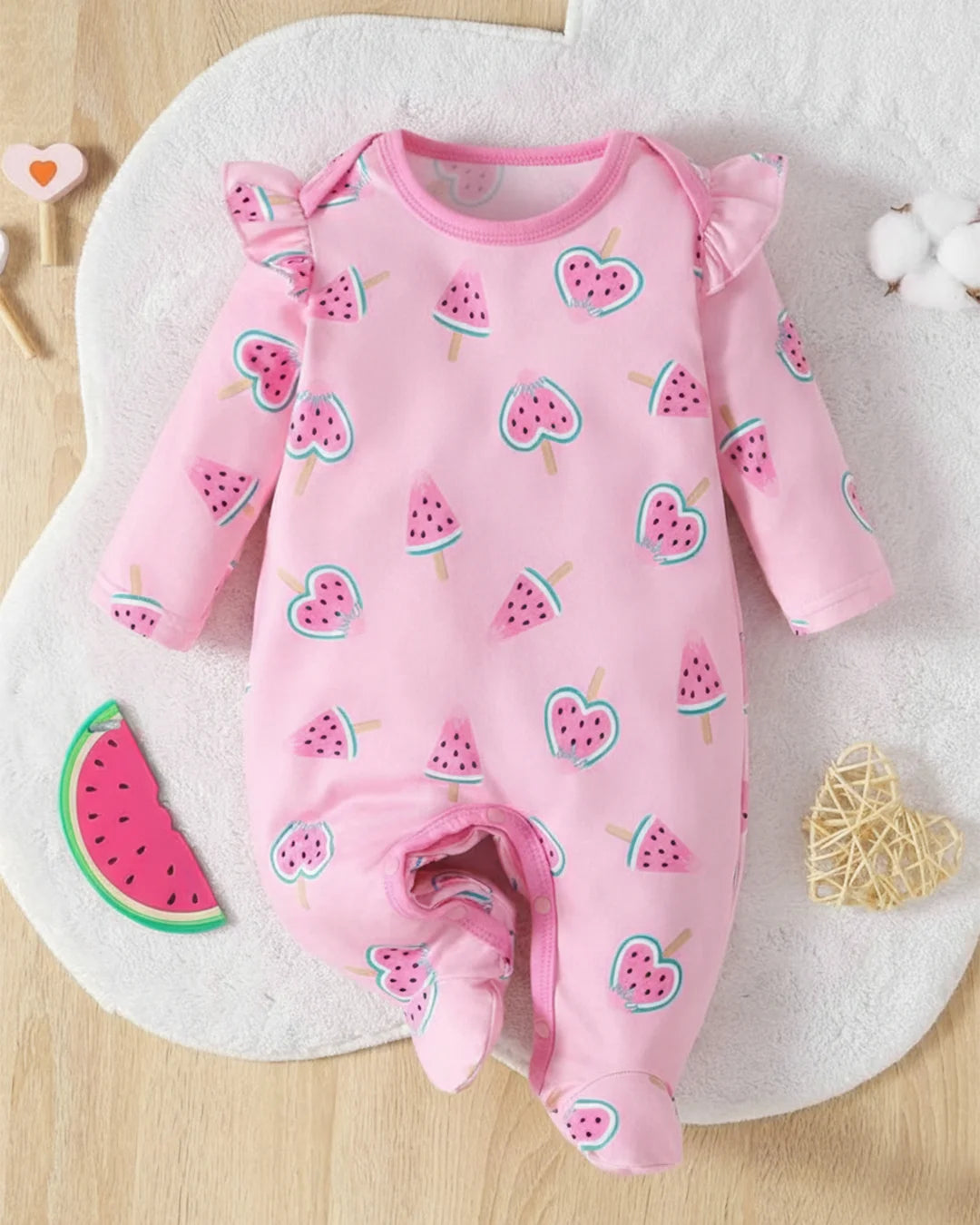 Pink baby onesie with watermelon pattern on a wooden surface