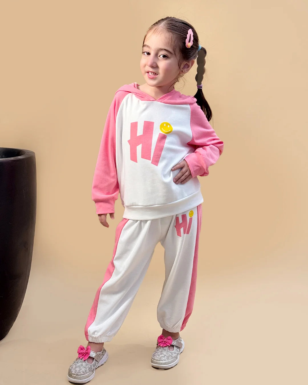Child wearing a pink and white outfit with 'Hi' print on a beige background