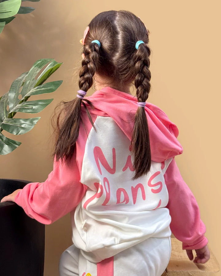 Child wearing a pink hoodie with 'No Plans' text, standing against a beige wall.