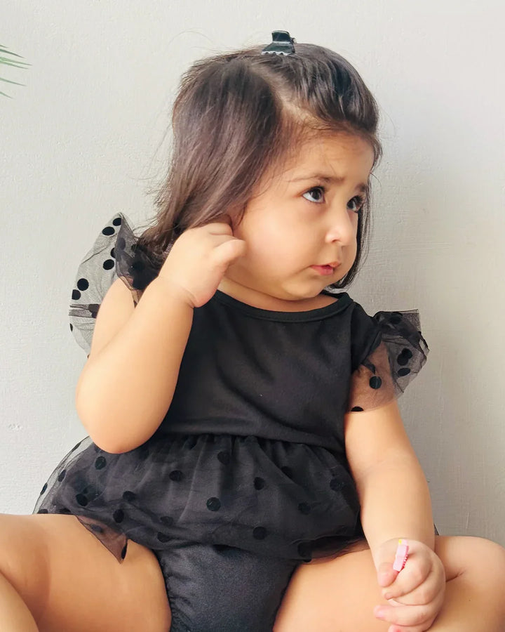 Child wearing a black outfit with sheer sleeves against a neutral background