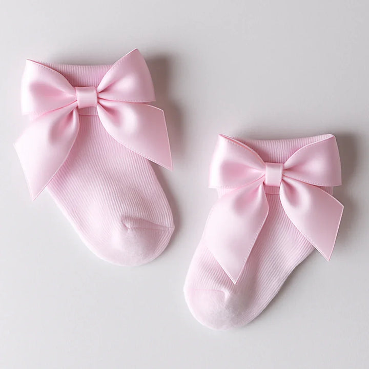 Two pink socks with large bows on a light gray background