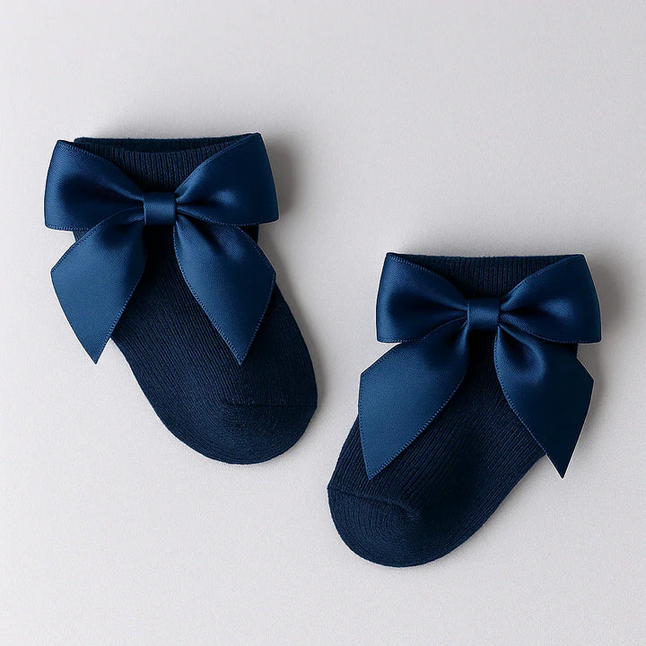 Pair of navy blue slippers with large satin bows on a light gray background