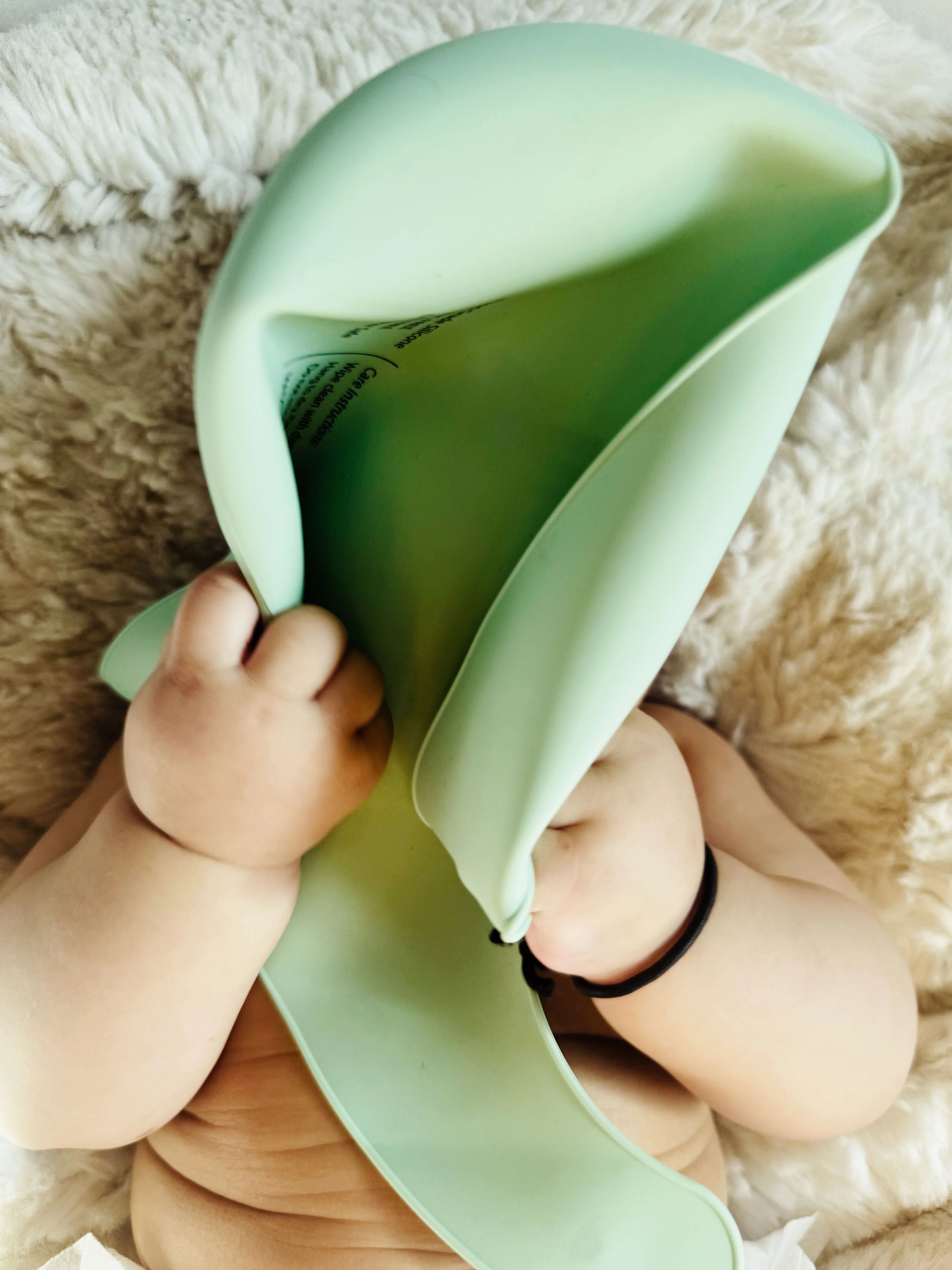 Baby playing with a green toy on a soft surface